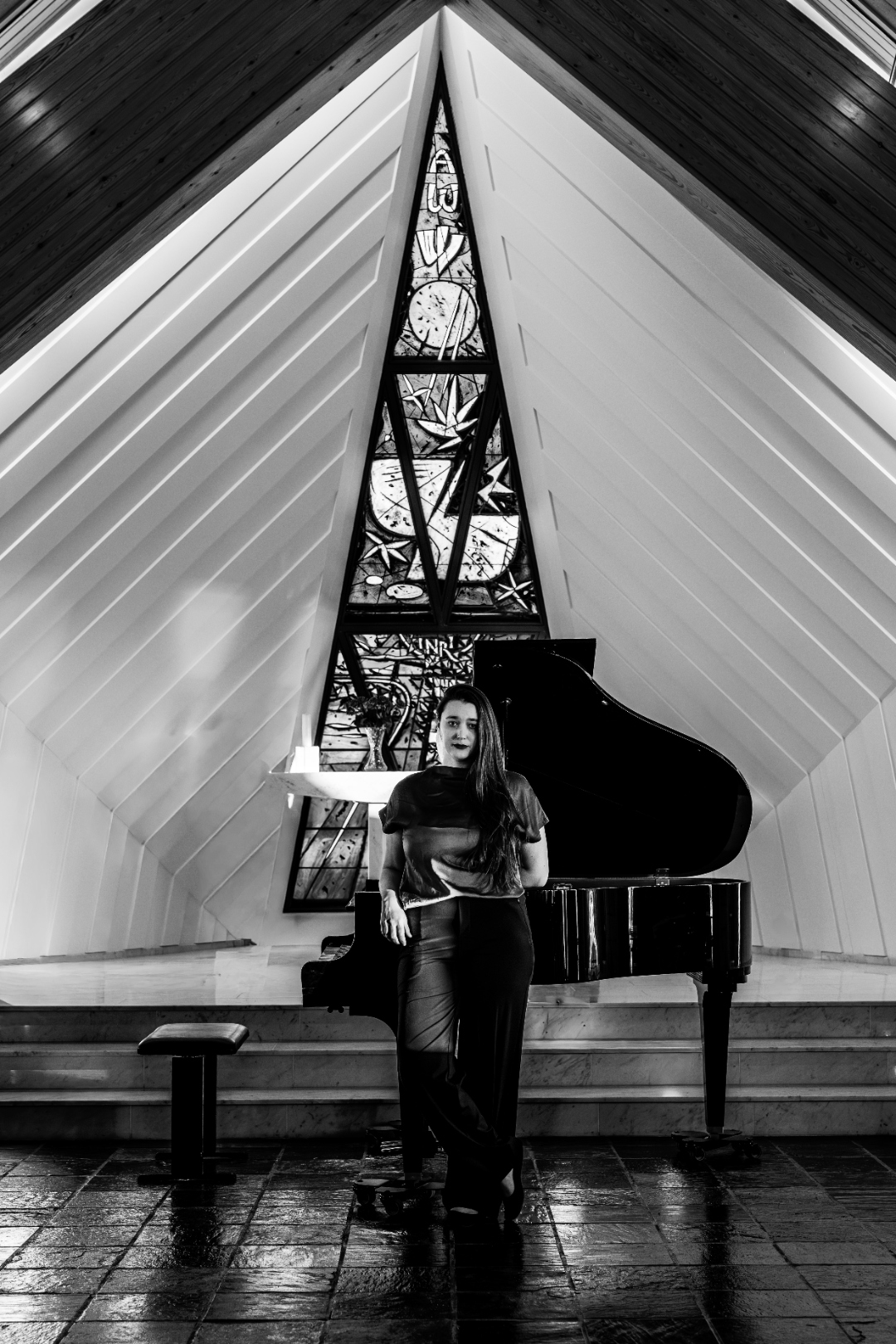 Heather Pinkham standing beside a grand piano, black and white